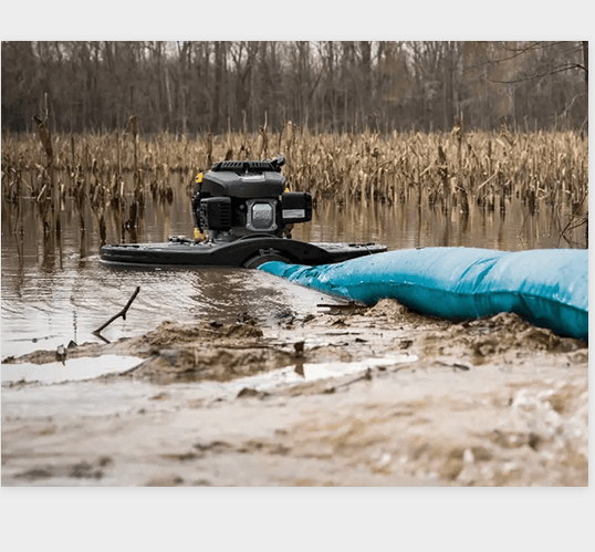 Warthog pump floating in a marsh, connected to a lay-flat hose